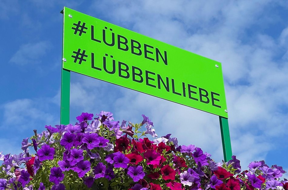 Ortsschild in Lübben und darunter pinke und lila Blumen