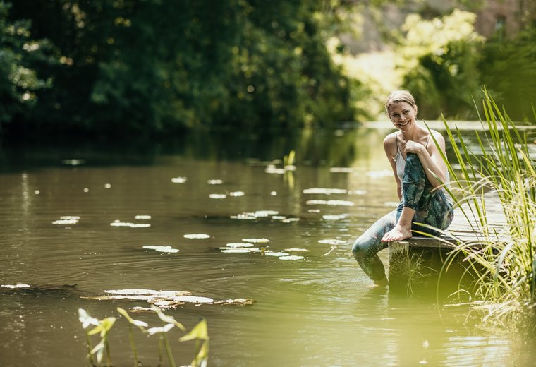 Frau sitzt nach Yoga in Sportkleidung am Fließ im Spreewald und entspannt