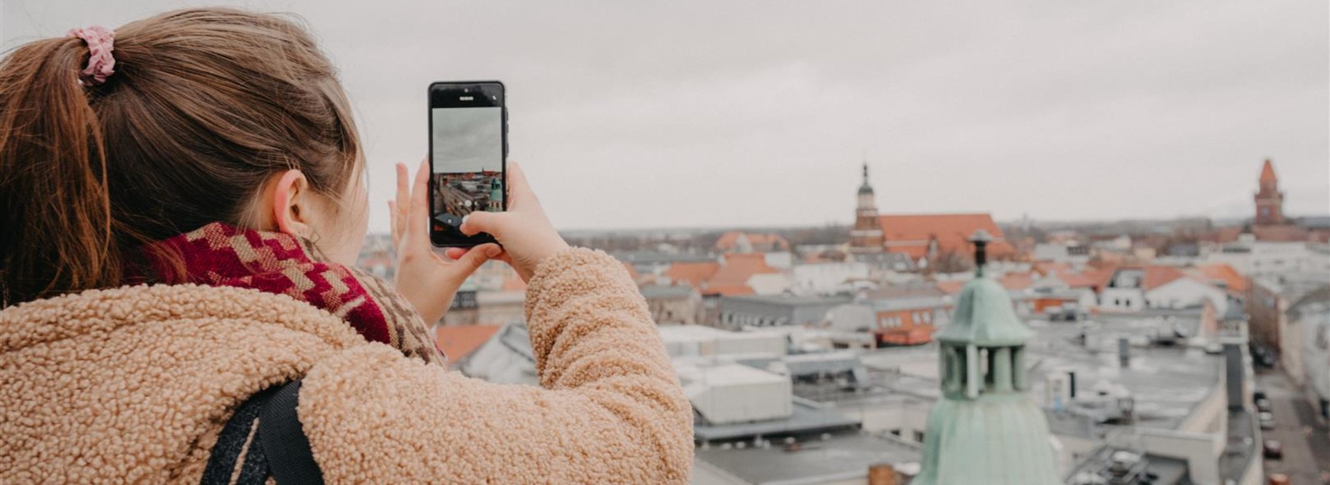 Frau fotografiert mit Handy die Stadt Cottbus von einem Aussichtsturm aus