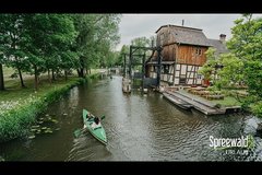 Fließ mit grünem Paddelboot und Mühle im Hintergrund