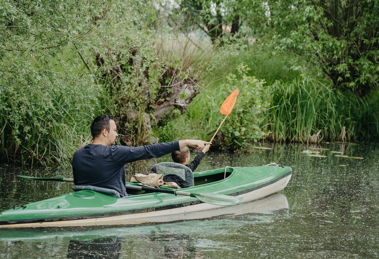Mann mit Kind paddelt im grünen Boot im Spreewald