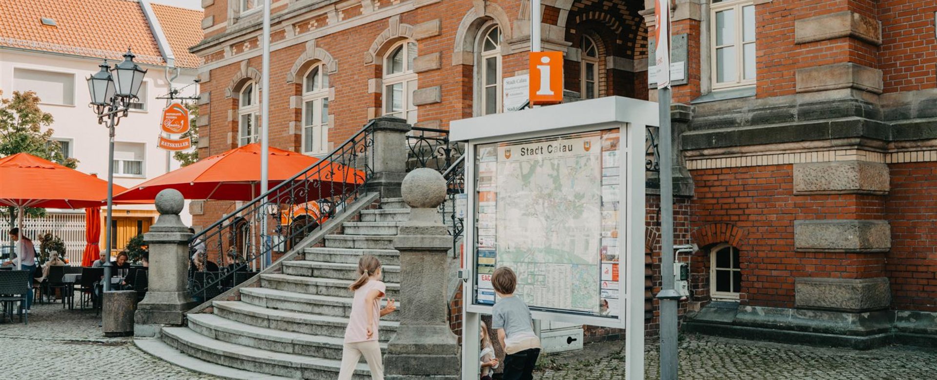 Kinder stehen vor Ortsinformation und spielen hinter dem Infoschild Verstecken