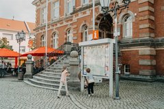 Kinder stehen vor Ortsinformation und spielen hinter dem Infoschild Verstecken
