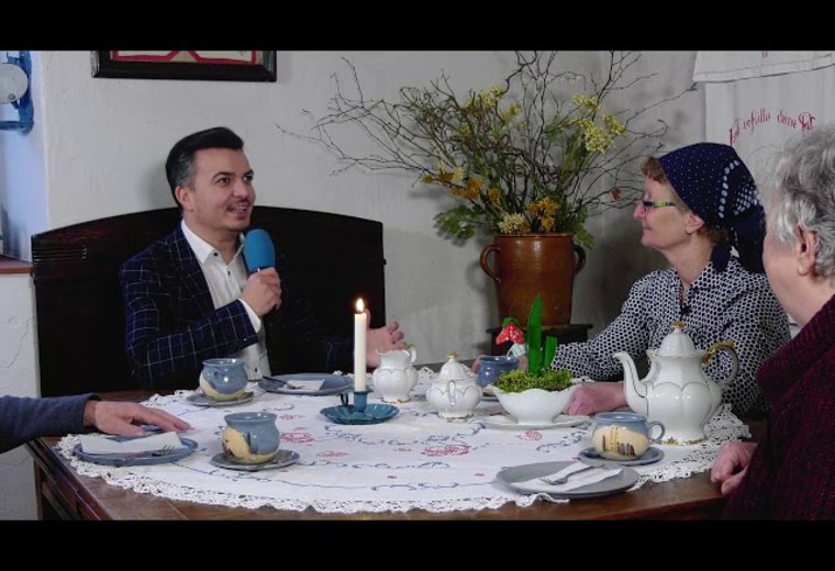 Moderator sitzt am Kaffeetisch in Museum und unterhält sich mit 2 älteren Damen