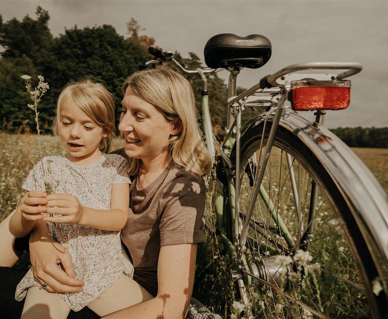 Frau hält Mädchen vor stehendem Fahrrad auf Feld