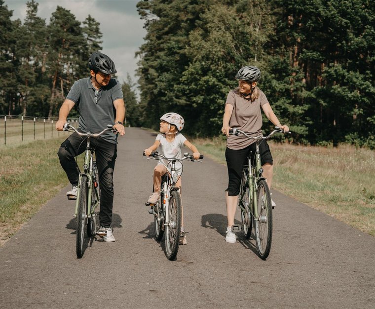 Mann links Kind Mitte Frau rechts fahren Rad und schauen sich dabei an