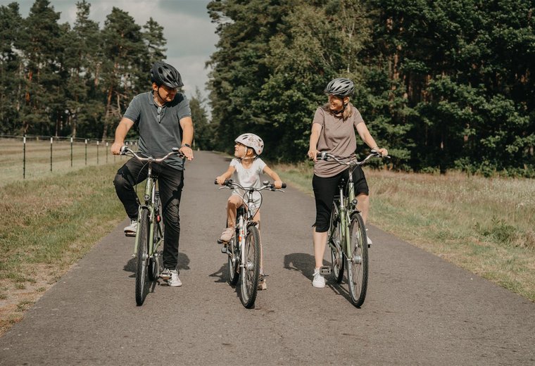 Mann links Kind Mitte Frau rechts fahren Rad und schauen sich dabei an