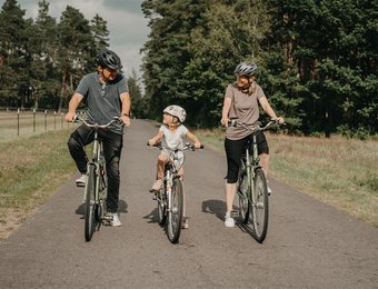 Mann links Kind Mitte Frau rechts fahren Rad und schauen sich dabei an