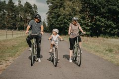 Mann links Kind Mitte Frau rechts fahren Rad und schauen sich dabei an