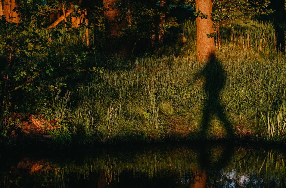 Person wirft Schatten auf gegenüberliegendes Ufer bei Sonnenuntergang