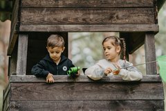 Mädchen und Junge in Jägerhochstand schauen raus und halten Blumen
